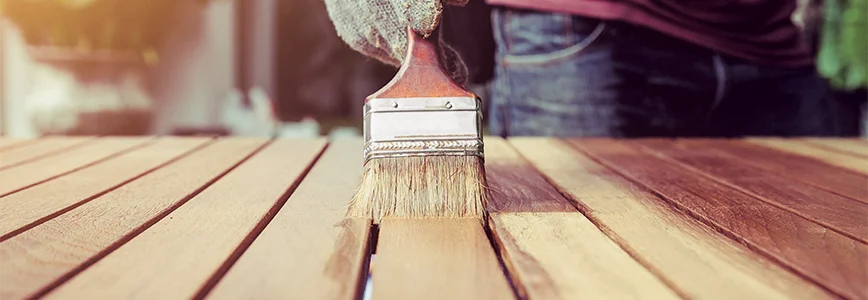 Person streicht Holzlatten mit Pinsel